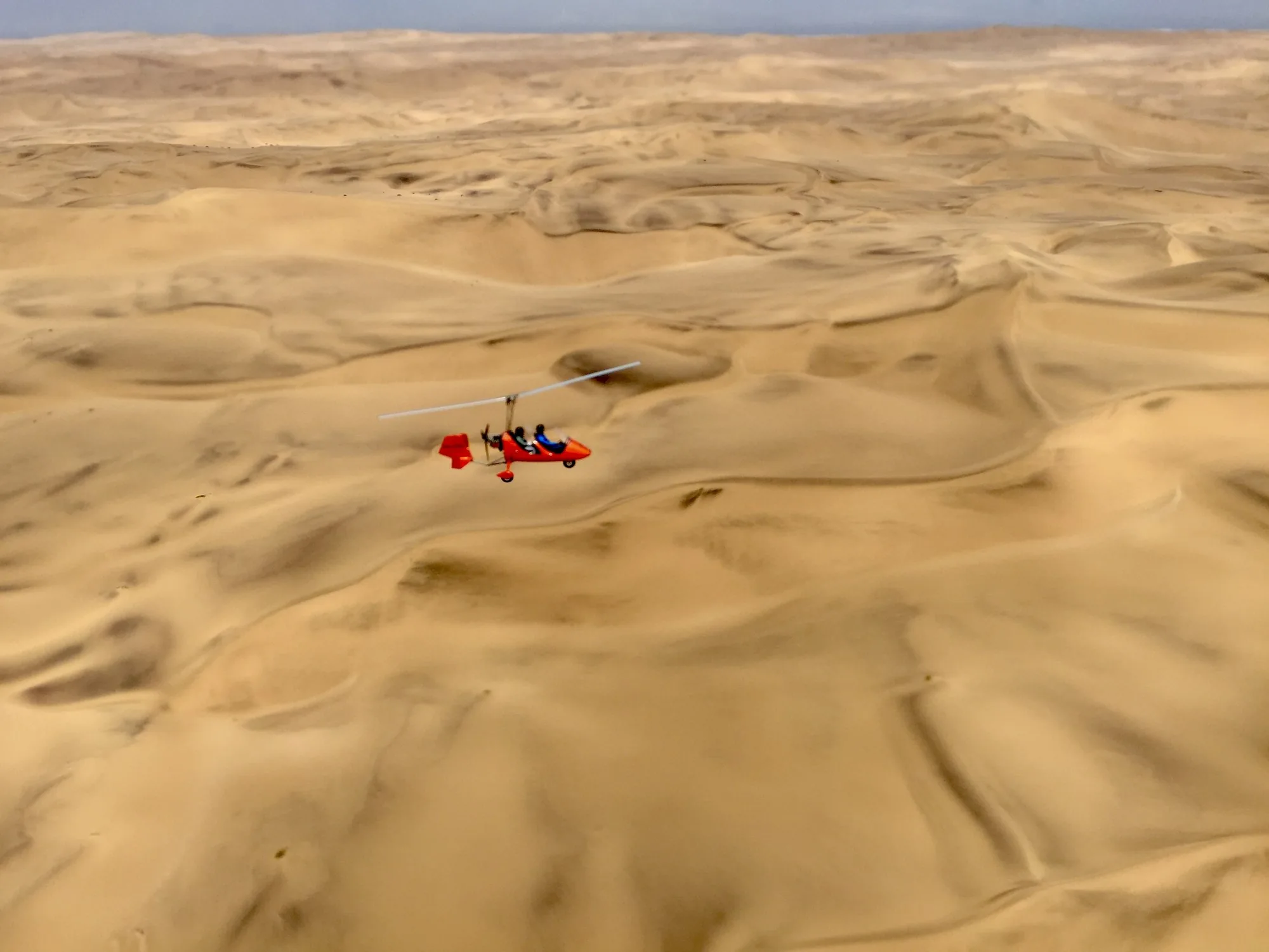 Roter Gyrocopter im Flug über den Dünen der Namib