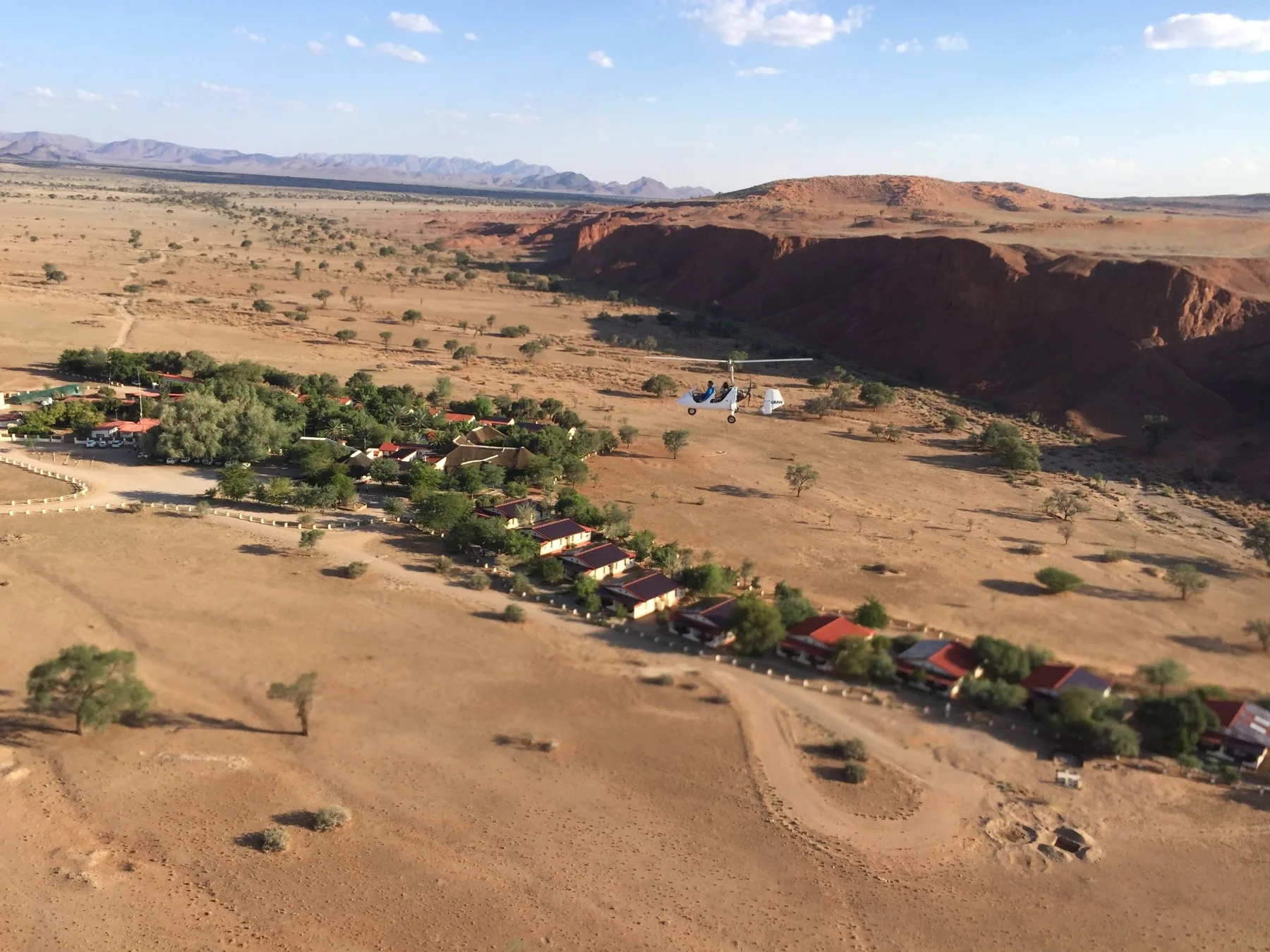 Gyro im Flug über einer Lodge neben roten Felsen in Namibia